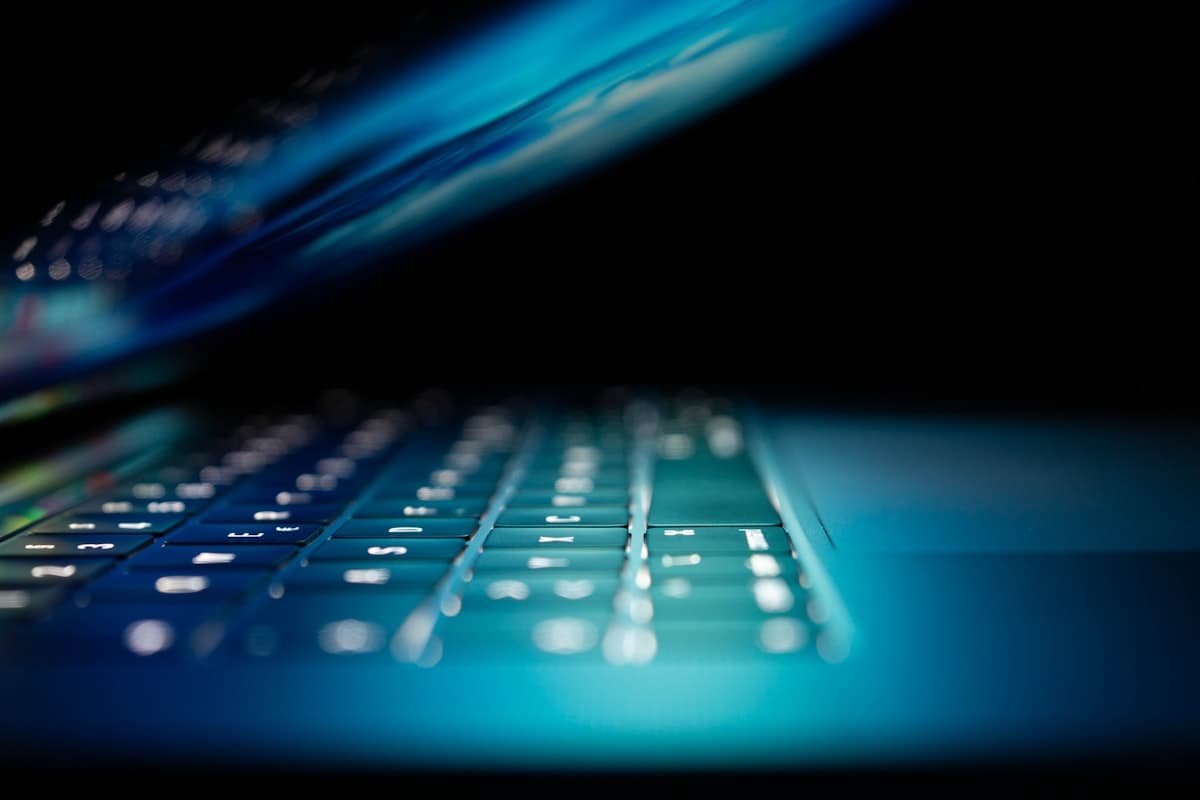 Backlit laptop keyboard glowing blue in a darkened room