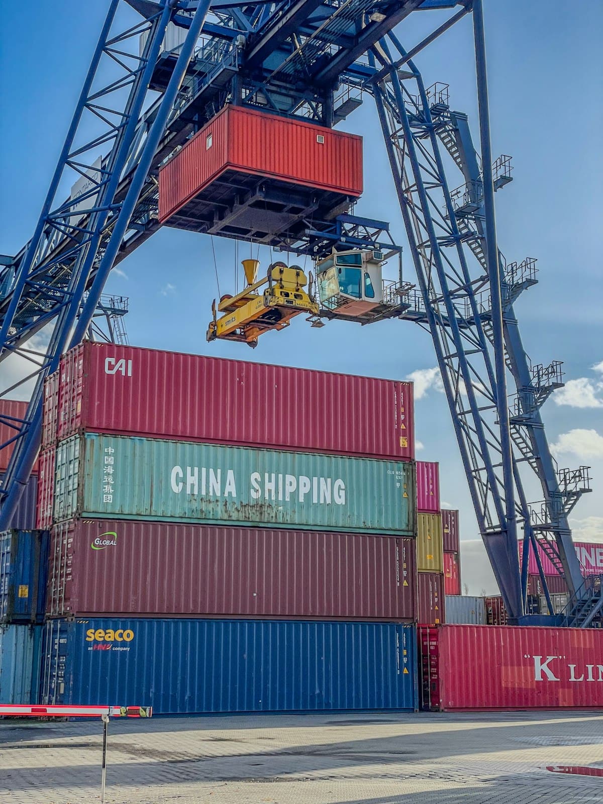 Gantry crane lifting a shipping container above a stacked yard